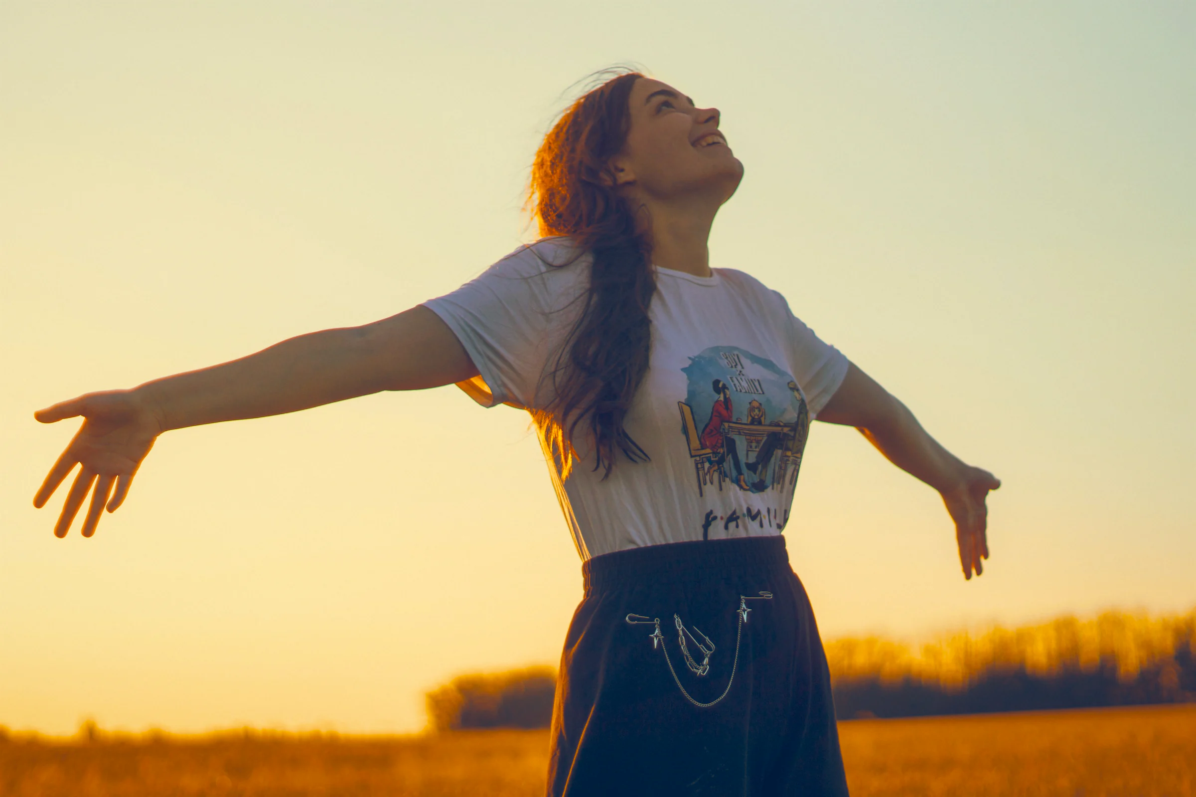 A young woman with her arms open, face turned up to a warm evening sky.